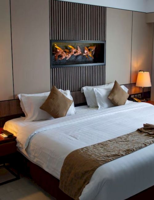 A cozy hotel room features a large bed with brown accents, bedside tables, lamps, and a decorative wall piece above the headboard.