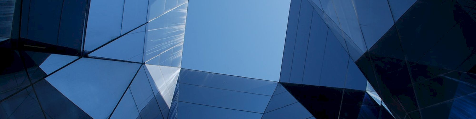 The image shows a geometric architectural structure with reflective glass panels forming a polygonal opening to the sky.