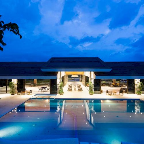 A luxurious outdoor pool area with a modern building, lit up beautifully against a twilight sky, creating a serene and inviting ambiance.