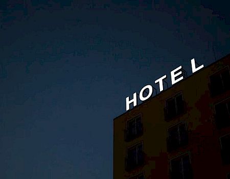 The image shows a building at night with a bright "HOTEL" sign on the rooftop.