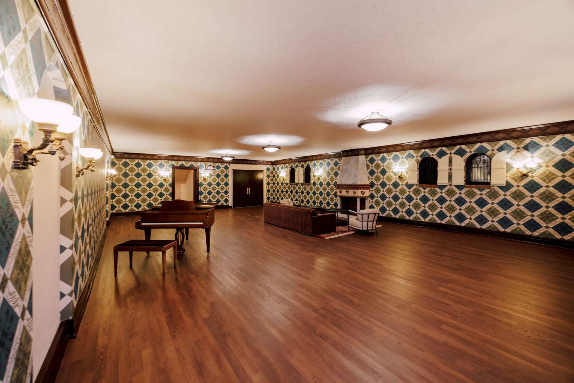 A spacious, elegantly decorated room with wooden floors, a piano, seating area, patterned walls, and ceiling lights.