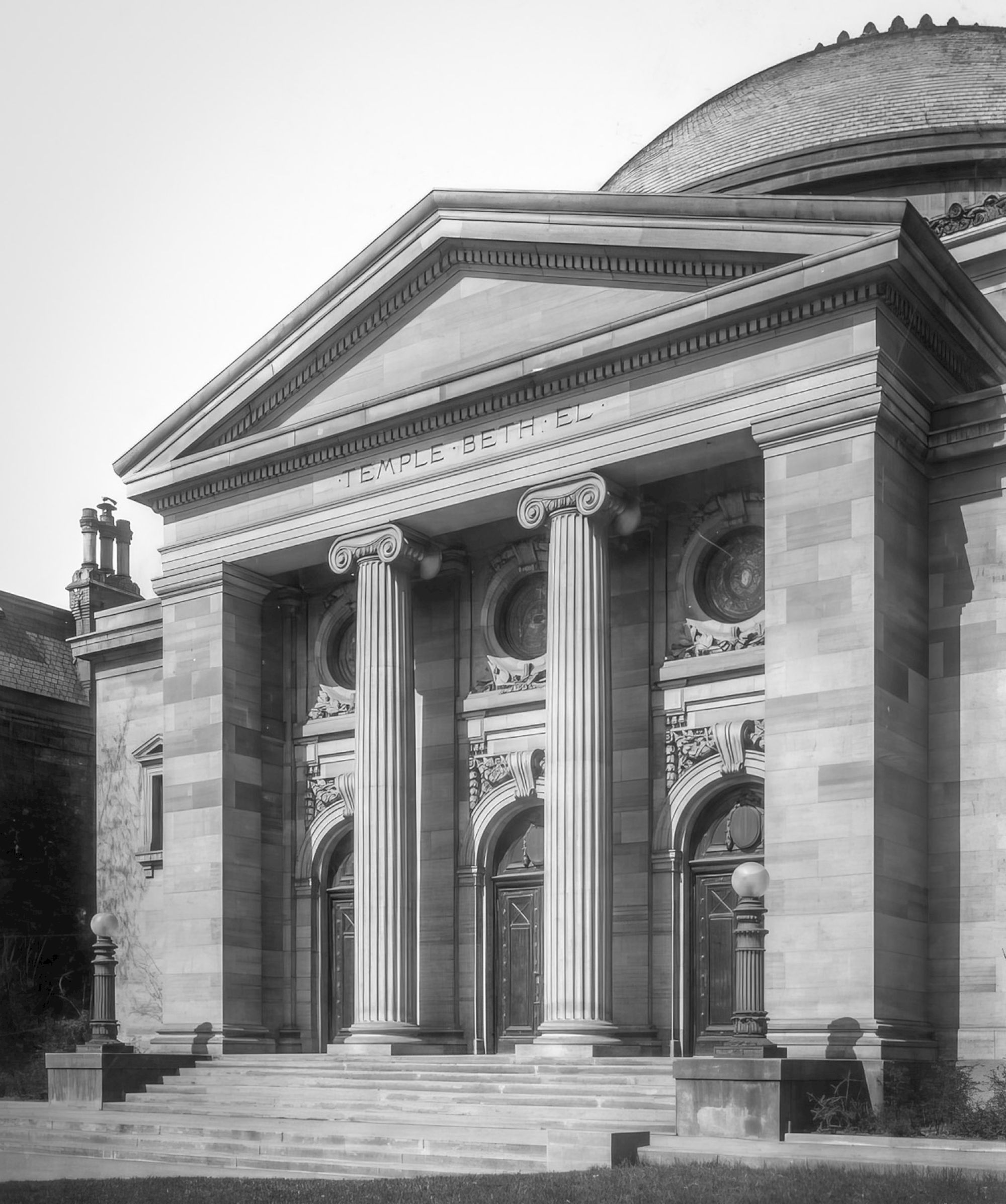 The image shows a classical building facade with columns and arched doorways, featuring neoclassical architecture.
