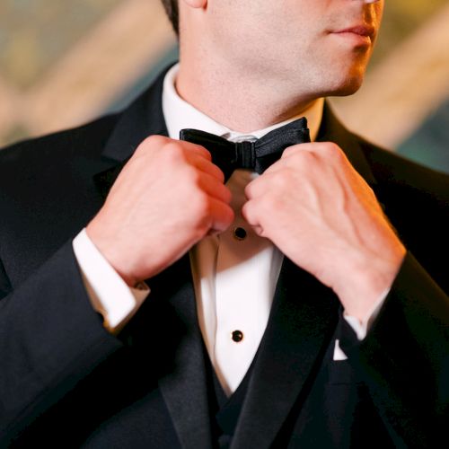 A person in a tuxedo adjusts their bow tie, focusing on hands and upper body.