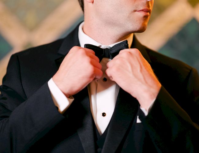 A person in a tuxedo adjusts their bow tie, focusing on hands and upper body.