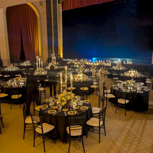 The image shows an elegantly set up banquet hall with round tables, black chairs, candles, and floral arrangements, ready for an event.