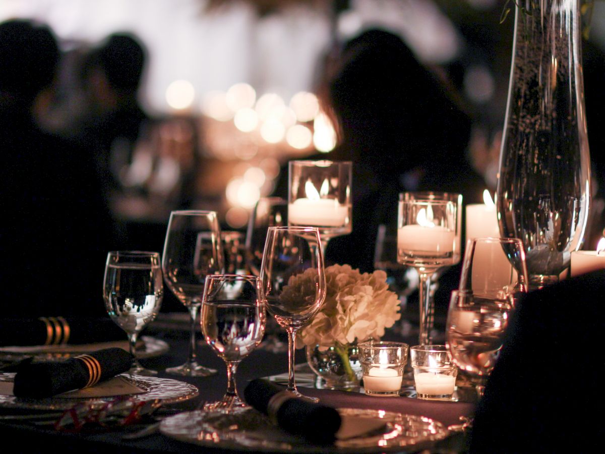 A dimly lit elegant dining setting featuring glassware, candles, and floral arrangements on a table, creating an intimate atmosphere.