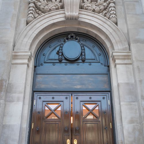 A grand wooden door with intricate carvings and gold handles, set in an ornate stone archway with decorative elements above.