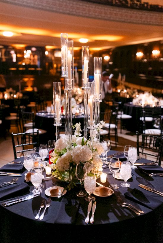 A beautifully set formal dining table features elegant floral arrangements and tall candles, with a dimly lit, sophisticated ambiance.