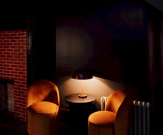 A cozy corner with two orange chairs, a small round table with a lamp, near a brick fireplace and a patterned rug on the wooden floor.