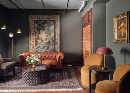A cozy living room with a leather sofa, patterned rug, round table, art on walls, and ambient lighting.