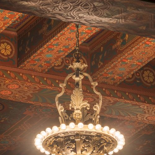 An ornate chandelier is hanging from a richly decorated ceiling featuring intricate patterns and designs.