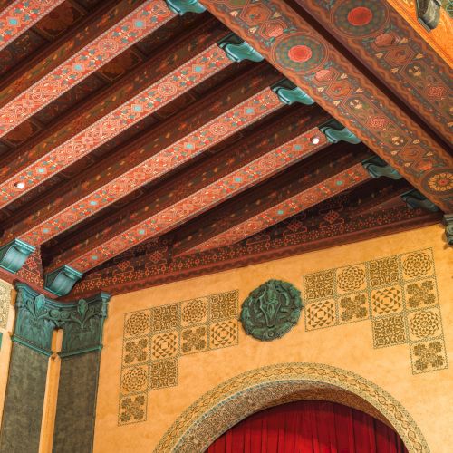 Ornate ceiling with decorative beams, intricate carvings, and red drapery below, showing a mix of geometric and floral patterns.