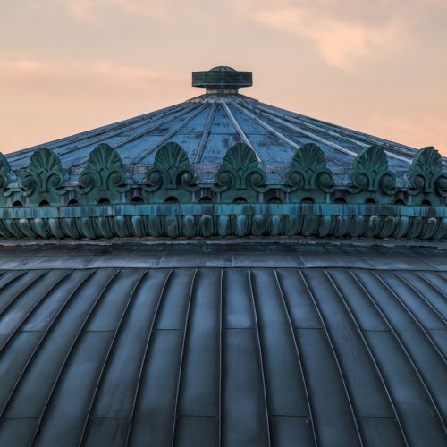 The image shows a detailed, ornate dome with a decorative finial, set against a soft, cloudy sky at dusk.