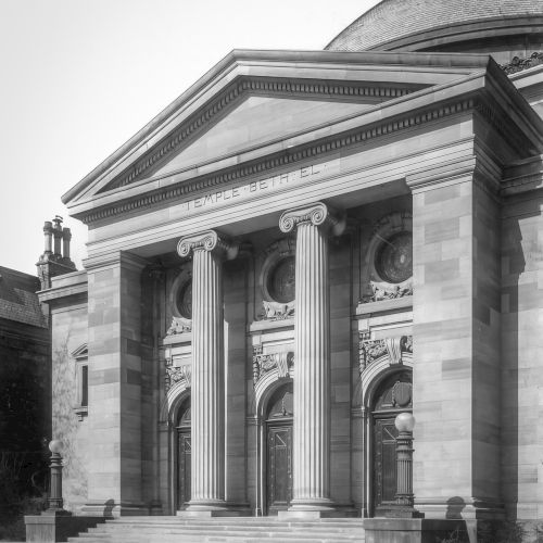 A neoclassical building with a columned entrance, featuring three ornate doors and a triangular pediment above.