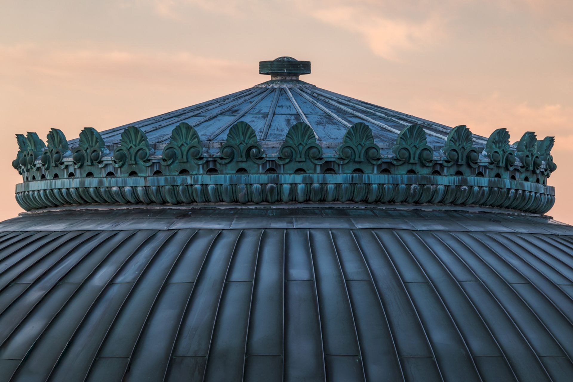 A detailed close-up of a domed roof with ornate architectural features against a soft sky background.