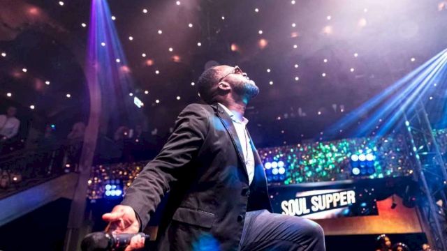 A suited singer holds a mic on a stage, spotlight beams overhead, with a &ldquo;SOUL SUPPER&rdquo; sign in the back.