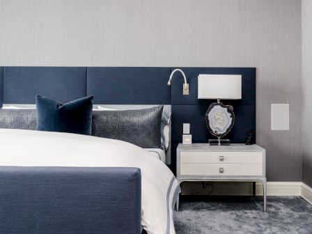 A modern bedroom with a blue and white color scheme, featuring a bed, nightstand, lamp, and decorative pillows, exuding elegance.